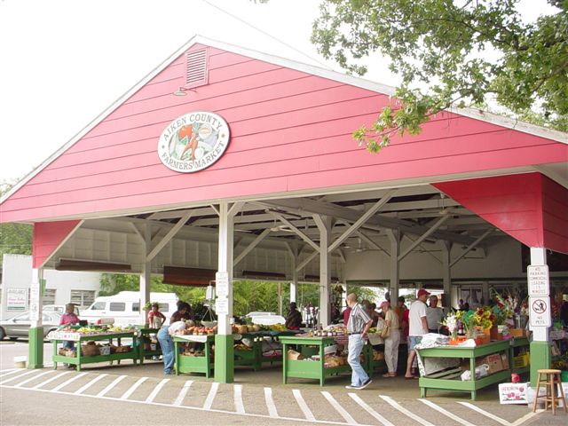 Vendors and shoppers under the red roof of the Aiken County Farmers Market